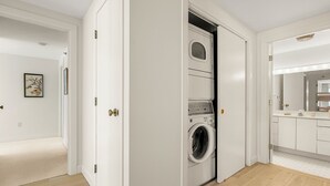 Ein Waschraum mit einer Frontlader-Waschmaschine und -trockner, Holzboden und ein Badezimmer mit Waschtisch und Spiegel.