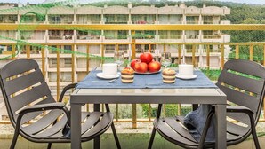 A table set with a white cup, a glass, a plate of apples, and a plate of pastries on a balcony with a view of a residential area. - Lovely apartment for 4 people with pool, WIFI, A/C, TV and terrace (Salou)
