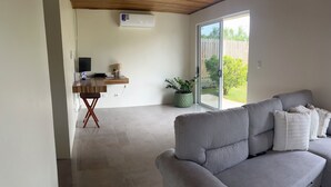 A modern living room with a grey sofa, a wooden desk, and a sliding glass door leading to an outdoor area. - Don Cidales House (Pocosol)