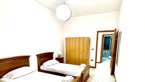 Una habitación con dos camas de madera, un armario, una lámpara y suelo de baldosas.