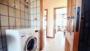 Un área de lavandería con una lavadora Whirlpool de carga frontal, una pared de azulejos y un pasillo que conduce a un comedor.