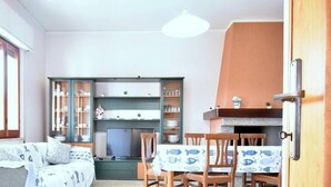 Un espacio habitable compacto con sofá, mesa de comedor, sillas, televisor y un mueble con estantes.