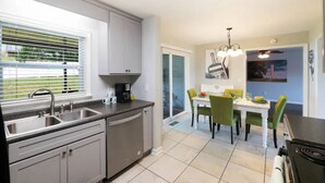 A modern kitchen with grey cabinets, a double sink, and a dining area with a white table and green chairs.