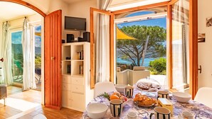 Ein Essbereich mit einem für das Frühstück gedecktem Tisch, einem Fernseher auf einem Regal und Blick aufs Meer.