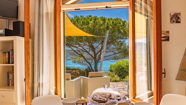 Ein Essbereich mit einem für das Frühstück gedecktem Tisch, Blick auf das Meer und einem Bücherregal im Hintergrund.