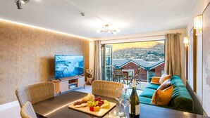 A modern hotel room with a dining area, a sofa, a television, and a scenic city view. - The Nugget-Free Parking-Direct Lake Access (Queenstown)