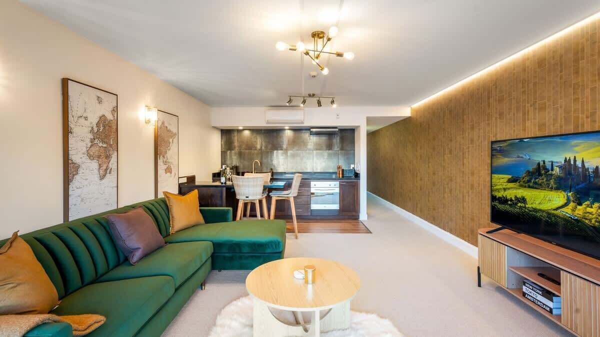 Een moderne woonkamer met een groene bank, een bijzettafeltje en een flatscreen televisie op een houten standaard.