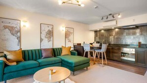 A modern living room with a green sofa, a round coffee table, and a dining area with a chair and table. - The Nugget-Free Parking-Direct Lake Access (Queenstown)