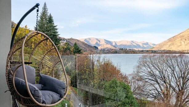 Une chaise en osier avec des coussins, une vue sur un lac et des montagnes en arrière-plan.