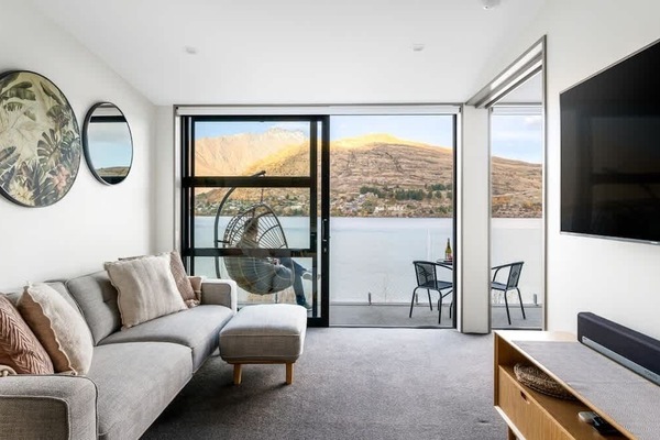 Stunning Lake and Mountain Views – Relax in this inviting living room, featuring a large flat-screen TV and expansive windows that showcase panoramic views of the lake and mountains, perfect for unwinding after a day of exploration.