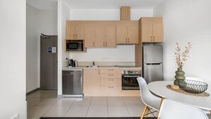 Une cuisine moderne avec des meubles en bois clair, des appareils en acier inoxydable et un coin repas comprenant une table et des chaises blanches.