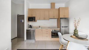 Une cuisine moderne avec des meubles en bois clair, des appareils en acier inoxydable et un coin repas comprenant une table et des chaises blanches.