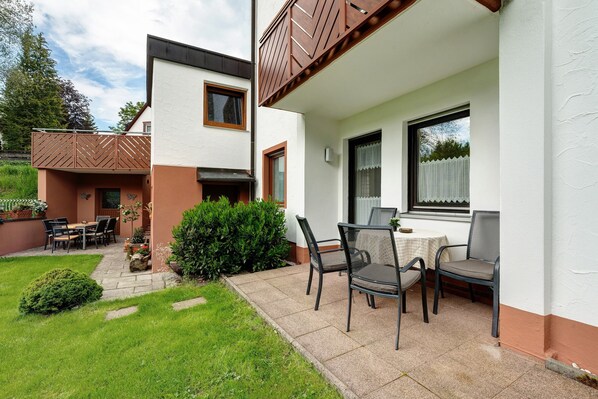 A patio with outdoor furniture, a small garden, and a building with a white exterior and brown accents.