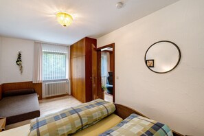 A bedroom with a bed, a wooden wardrobe, a radiator, and a window with curtains.