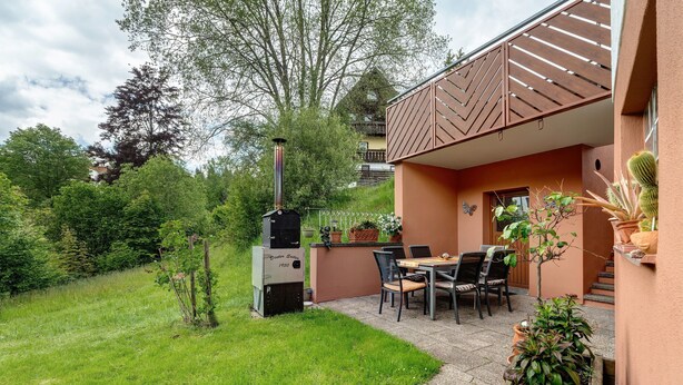 Une terrasse avec un barbecue, des sièges d’extérieur et des plantes en pot.