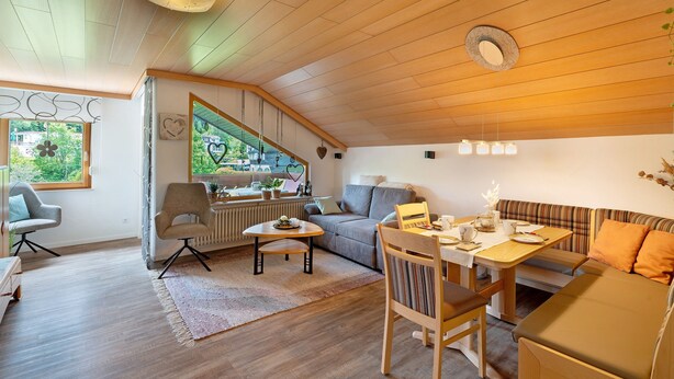 Una sala de estar acogedora con techo de madera, un sofá, una mesa de comedor y un ventanal con vistas.