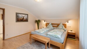 Un dormitorio con cama, mesitas de noche, un banco, un cuadro enmarco y una lámpara en el techo.