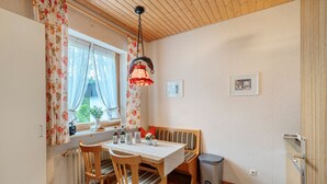 Un espace repas comprenant une table, des chaises, un banc, un luminaire suspendu, un radiateur et une poubelle.