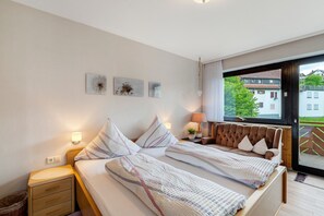 Une chambre à coucher avec un lit, des tables de chevet, une fenêtre donnant sur un paysage agréable et des œuvres d’art murales.