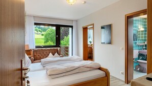 Une chambre à coucher avec un lit, une fenêtre, un balcon et une salle de bain visible à travers une porte ouverte.