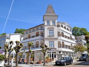 A multi-story building with a prominent tower, balconies, and a cafe area with outdoor seating.