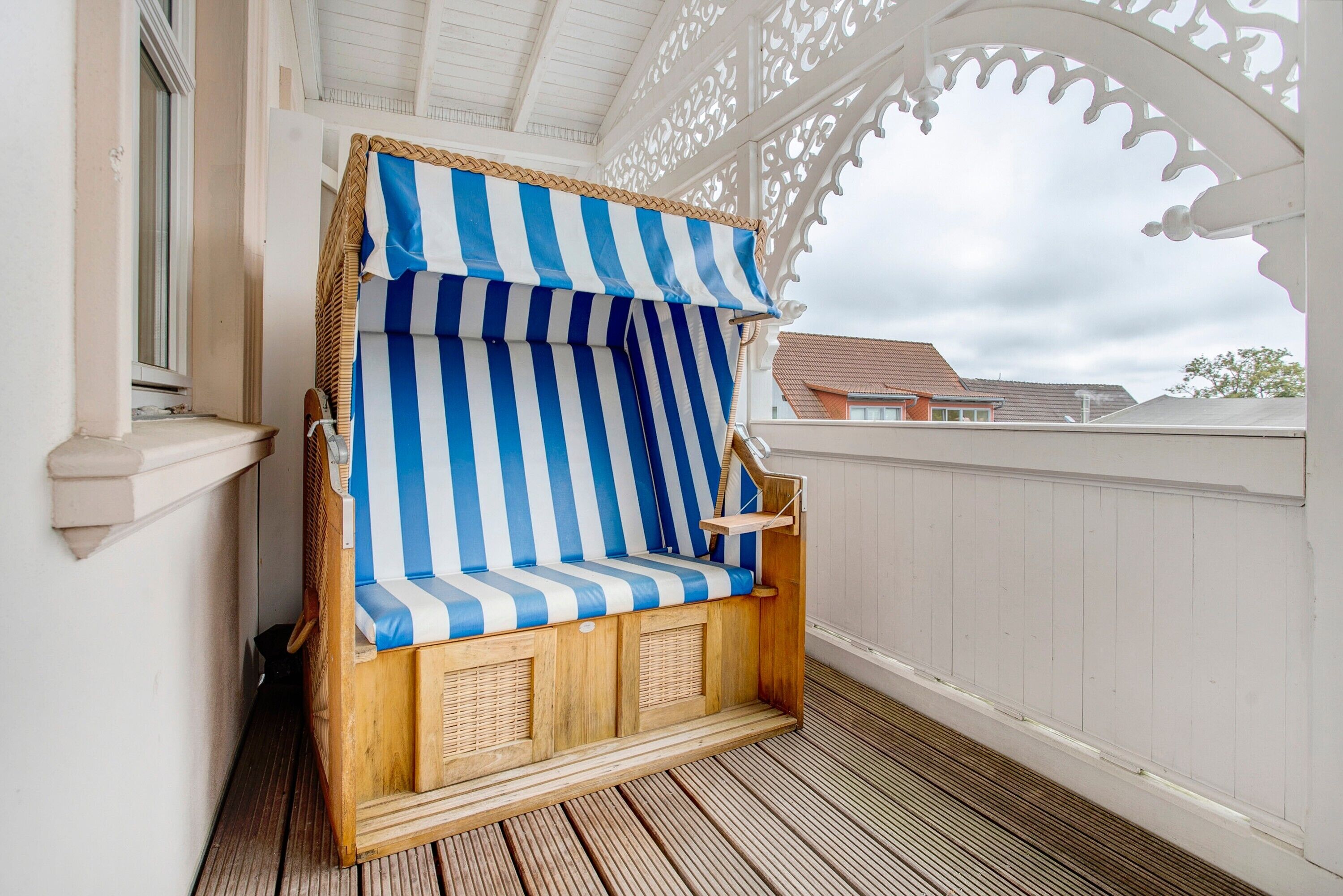 A wooden beach chair with blue and white stripes, a wooden floor, and a white fence.