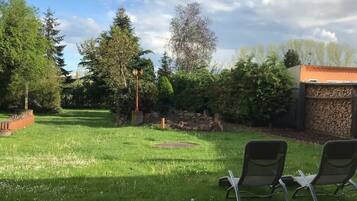Un espacio al aire libre con césped, dos sillones de descanso, un muro de piedra y árboles.