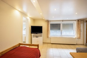 Ein Schlafzimmer mit einem Bett, einem Fernseher, einem Fenster mit Jalousien und einer Heizung.