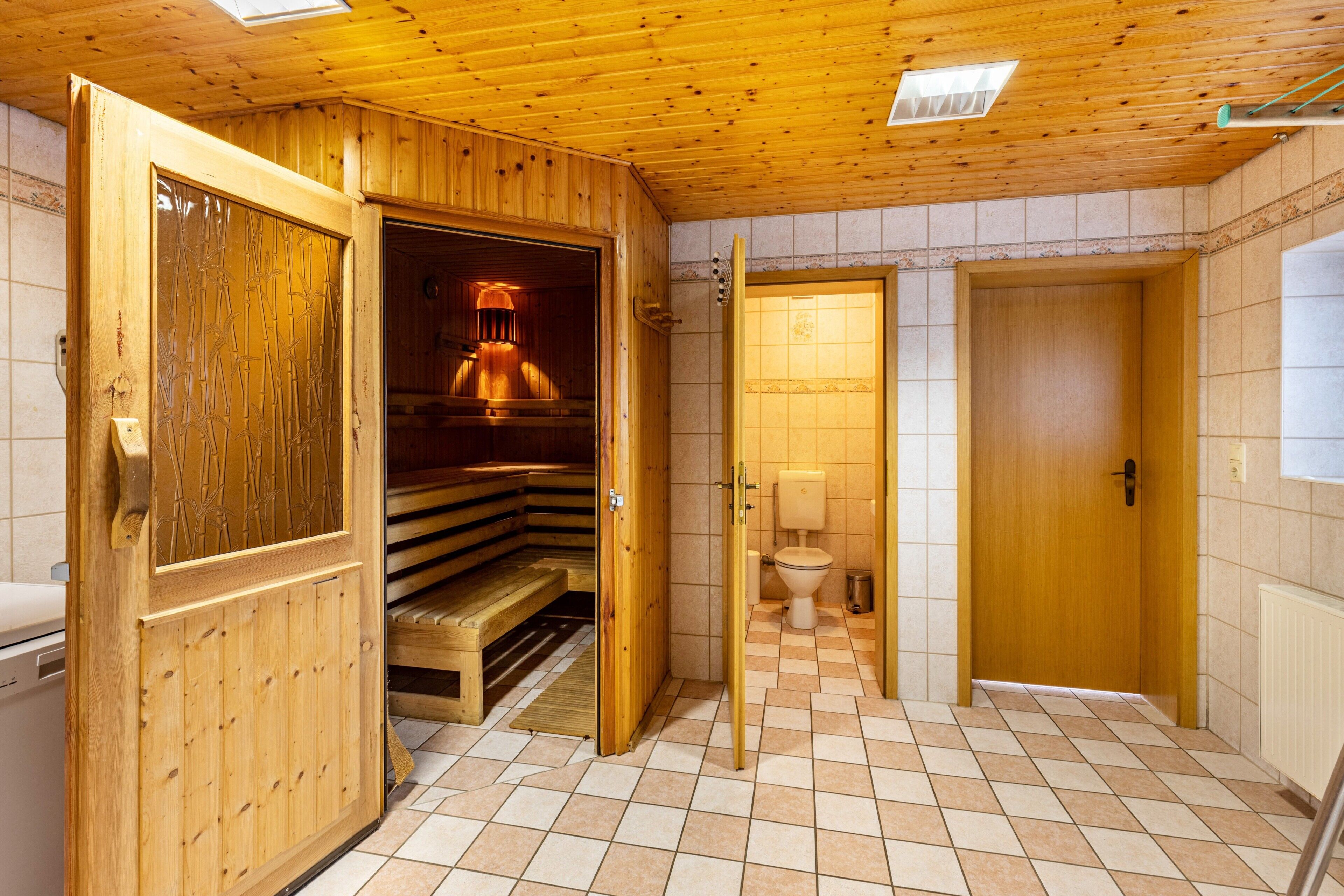 Ein Sauna Raum mit Holzwänden und Fliesenboden, eine Toilette und eine Holztür.