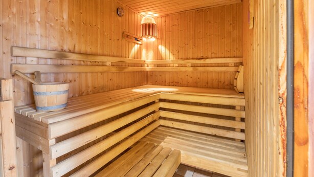 A wooden sauna with benches, a bucket, and a light fixture. - Apartment 'Ruhiges Nest Mit Sauna Und Garten' with Shared Garden and Wi-Fi (Jessen (Elster))