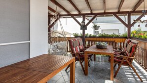 Un patio exterior con una mesa y sillas de madera, una silla colgante y vistas a un jardín.