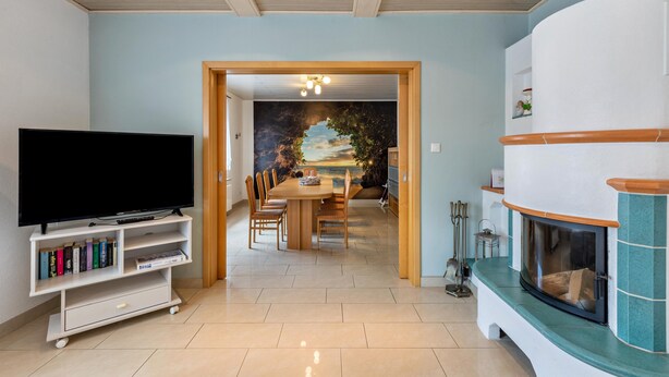 Una sala de estar con televisión, estantería, mesa de comedor, sillas y chimenea.