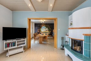 Ein Wohnzimmer mit Fernseher, Bücherregal, Esstisch, Stühlen und Kamin.