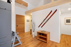 Ein modernes Interieur mit Holzboden, einem grauen Sofa, einer weißen Vase mit Zweigen und einem an der Wand befestigten Skiständer.