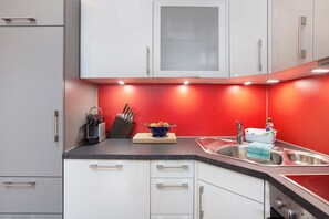 Une cuisine moderne avec des meubles blancs, un plan de travail rouge, un évier et une cuisinière.