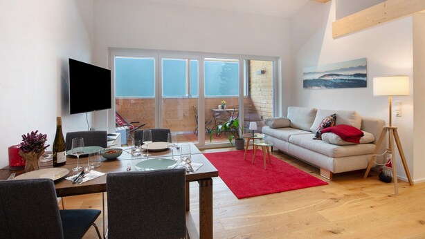 A modern living room with a dining area, a sofa, a TV, and a large window. - Apartment 'Hedi' with Mountain View, Balcony and Wi-Fi (Feldberg (Schwarzwald))