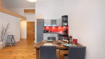 Eine moderne Küche mit grauen Schränken, einer roten Akzentwand und einem Essbereich mit grauen Stühlen und einem Holztisch.