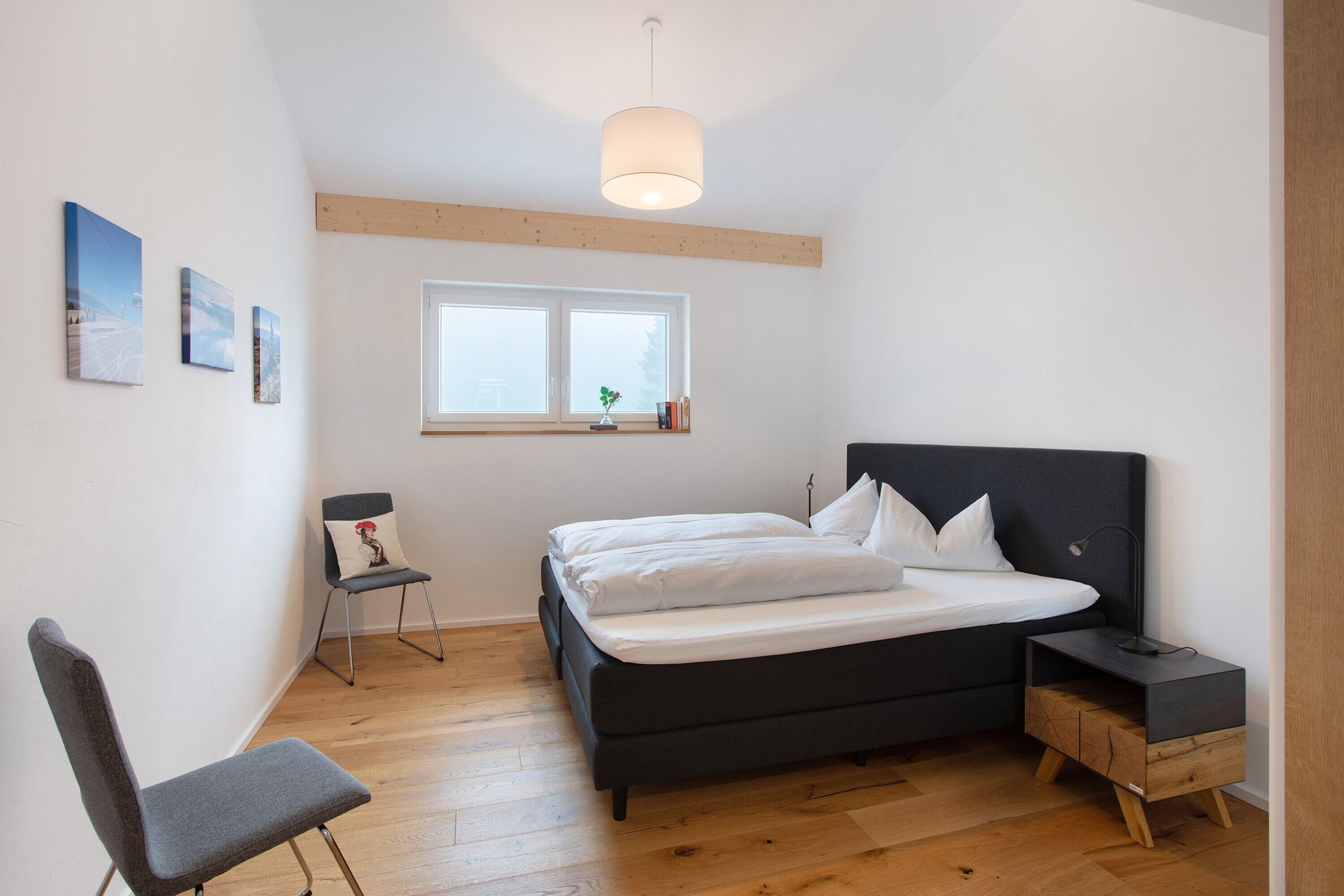 Une chambre à coucher comprenant un lit, une chaise, une table de chevet, une fenêtre et un luminaire au plafond.