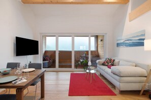 Un salon moderne comprenant un coin repas, un canapé, un tapis rouge et un téléviseur fixé au mur.