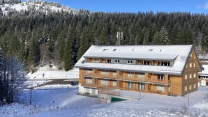 A modern building with a sloped roof, multiple windows, and a snow-covered landscape. - Apartment 'Hedi' with Mountain View, Balcony and Wi-Fi (Feldberg (Schwarzwald))