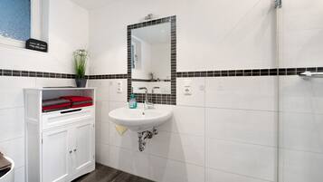 Une salle de bain avec un lavabo blanc, un miroir, une plante en pot et un meuble contenant une serviette rouge.