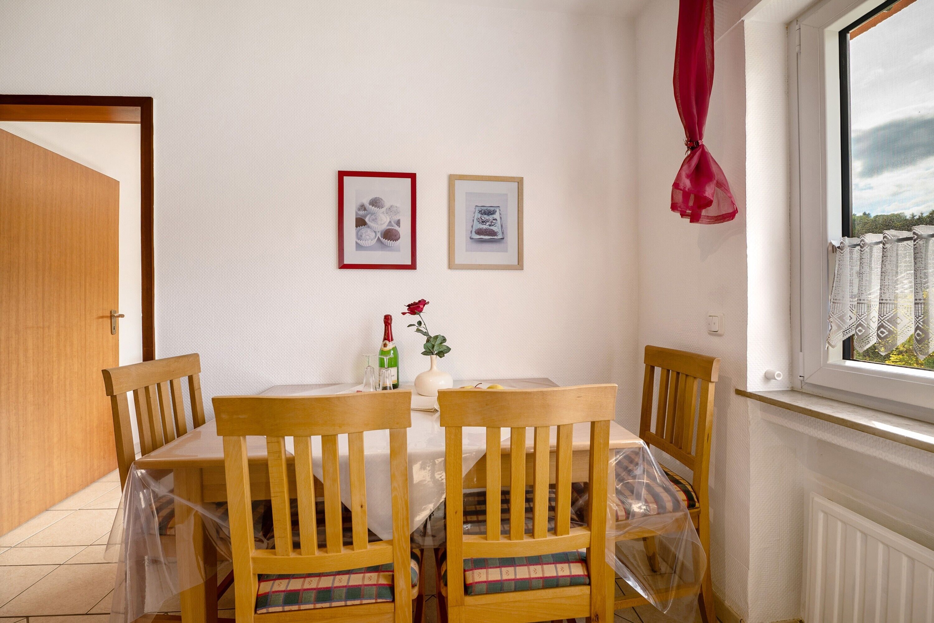 Un coin repas comprenant une table, des chaises, un vase avec une fleur et deux tableaux encadrés accrochés au mur.