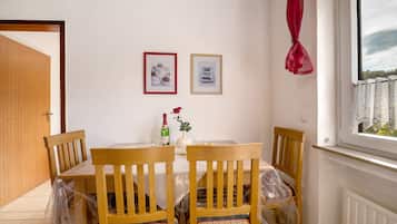 Un coin repas comprenant une table, des chaises, un vase avec une fleur et deux tableaux encadrés accrochés au mur.