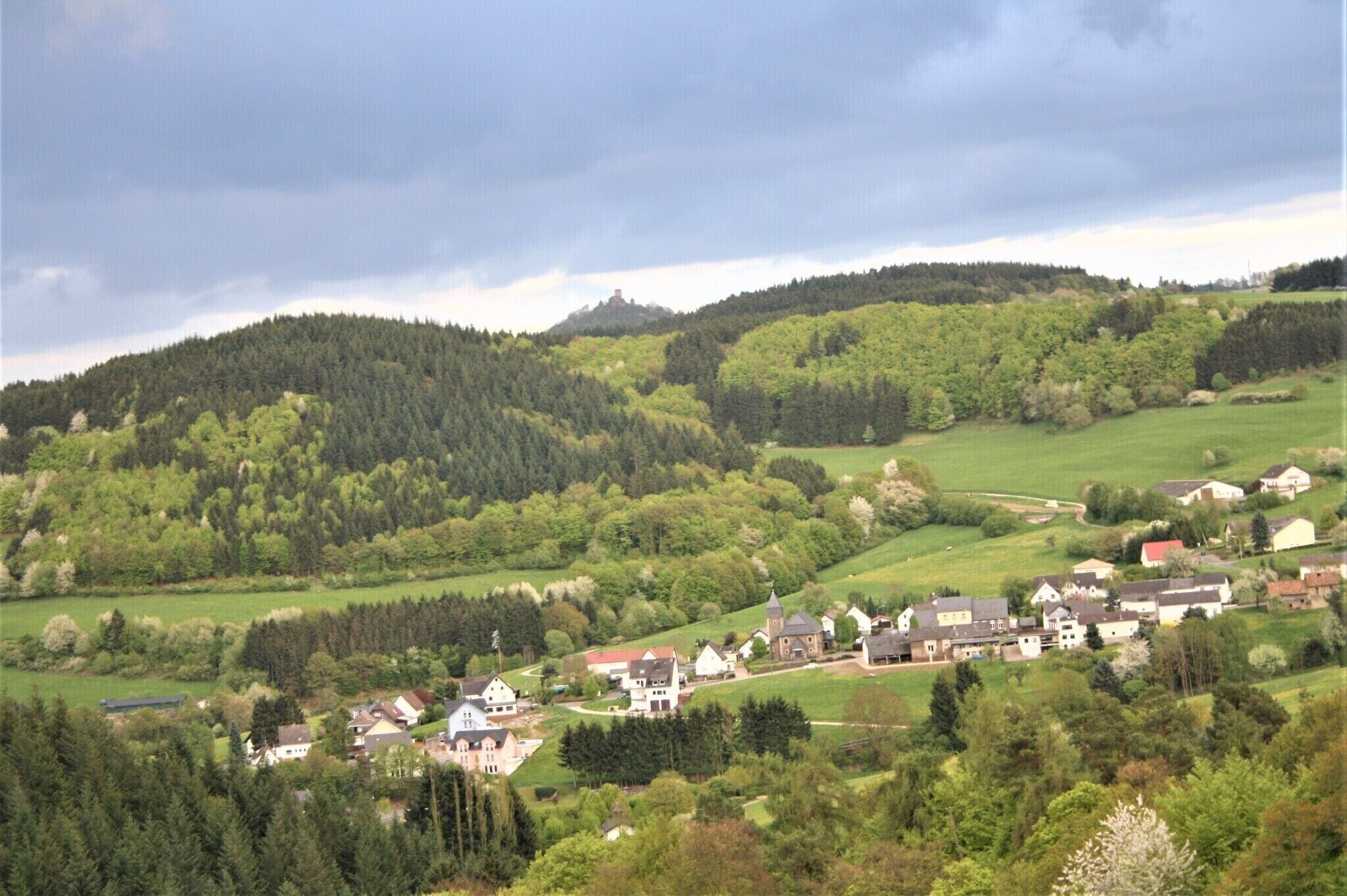 Ein ländliches Dorf mit Häusern, einer Kirche und einem Hügel mit dichtem Wald.