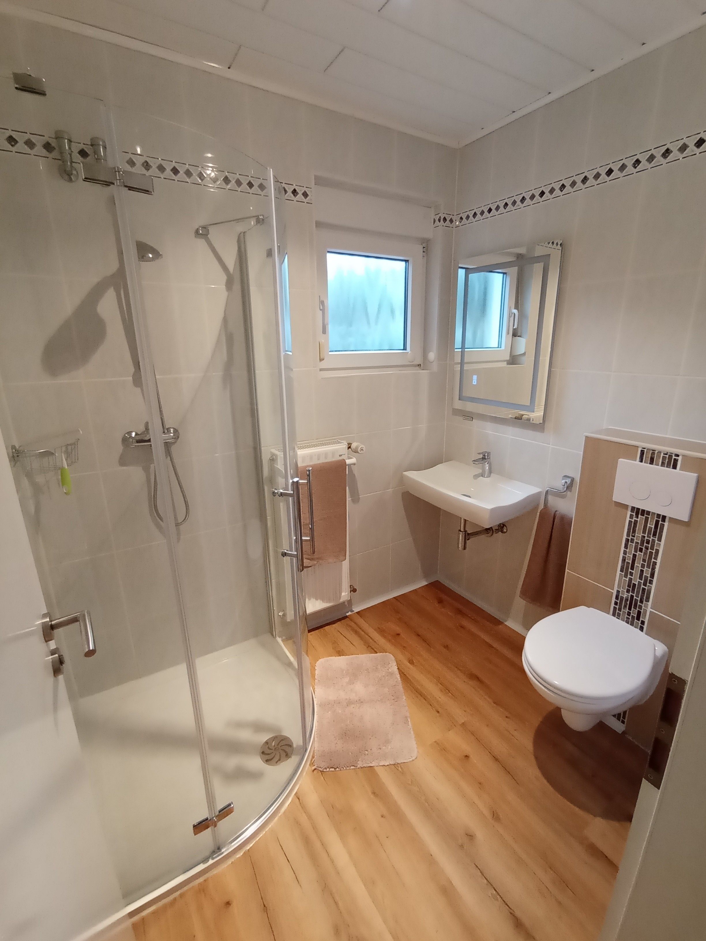 Un baño con ducha de vidrio, lavamanos, inodoro y ventana.