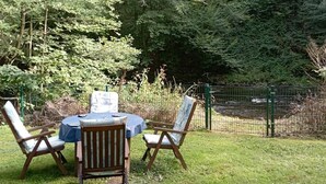 Un espacio al aire libre con mesa y sillas, rodeado de abundante vegetación y una cerca.