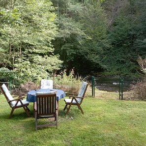 An outdoor seating area with a table and chairs, surrounded by lush greenery and a fence.