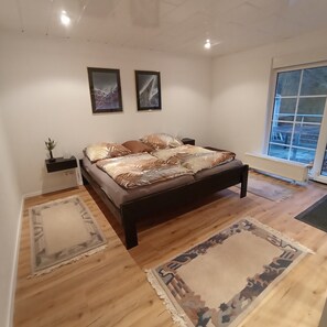 A bedroom with a bed, two framed pictures on the wall, a window, and a view of the outside.