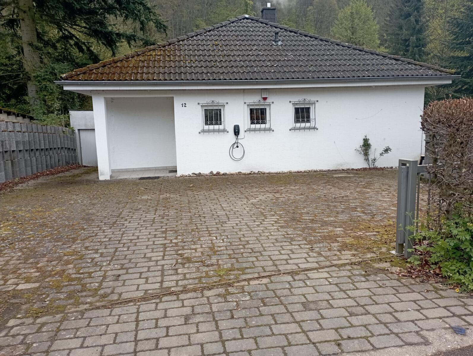 A single-story building with a tiled roof, a paved driveway, and a small fenced area.