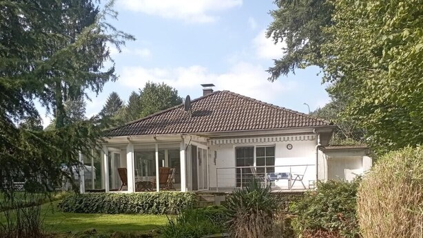 Una casa con porche cubierto, un estanque y follaje circundante.